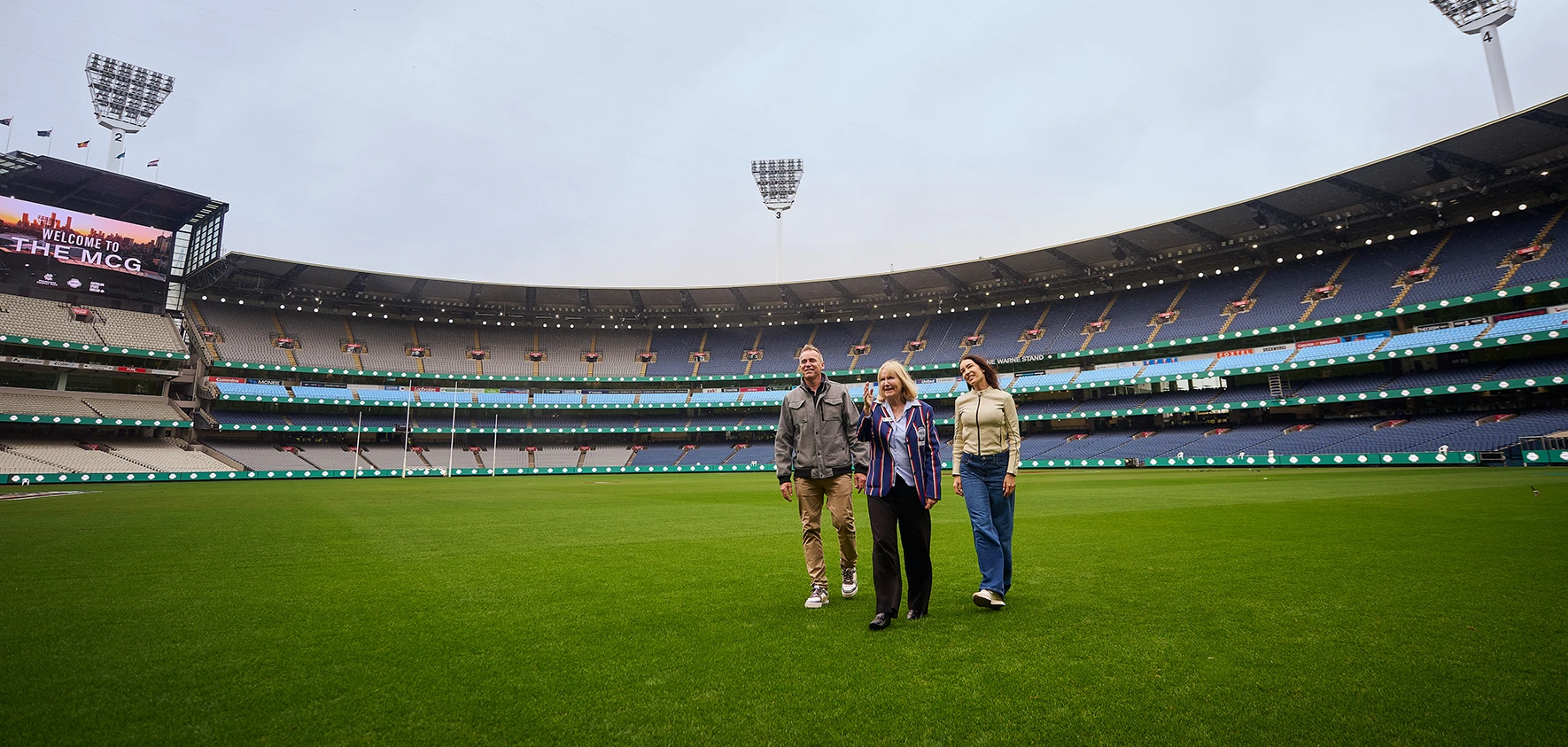 Group of 3 walk across the MCG turf during a stadium tour.