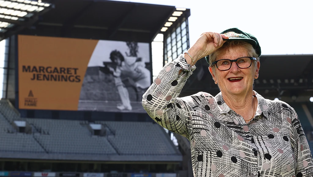 Marg Jennings stands in front of the MCG big screen wearing her baggy green cap