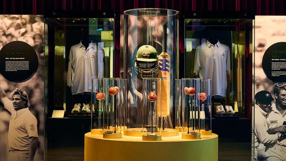 Shane Warne exhibition with cricket balls in a golden centre, surrounded by glass displays and red curtains.