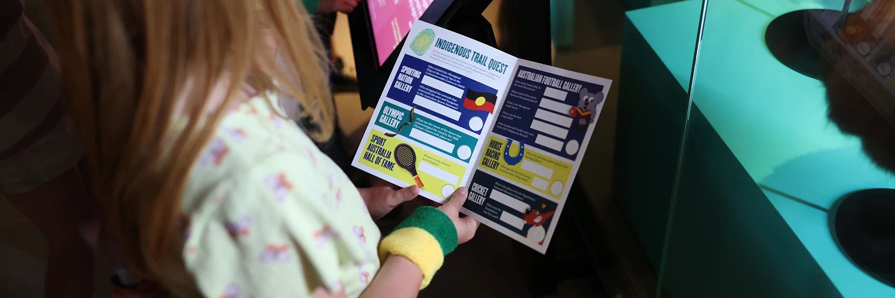 A child reads an Indigenous Trail booklet in front of museum display