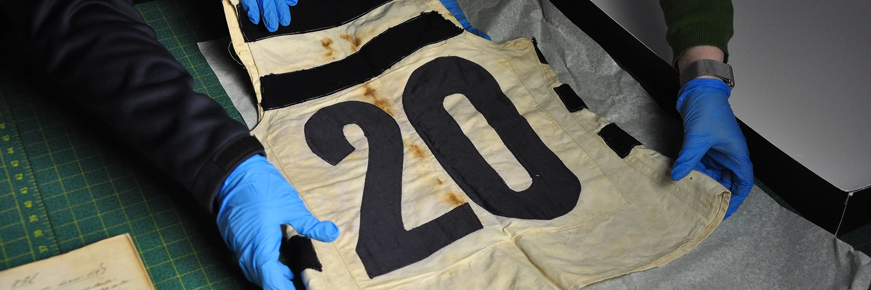 Gloved hands unfolding a vintage cream and black football guernsey numbered 20