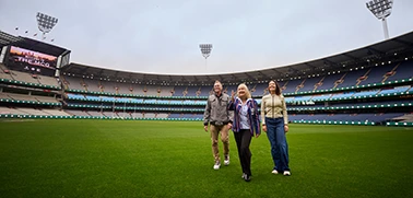 Group of 3 walks across the MCG turf during a stadium tour.