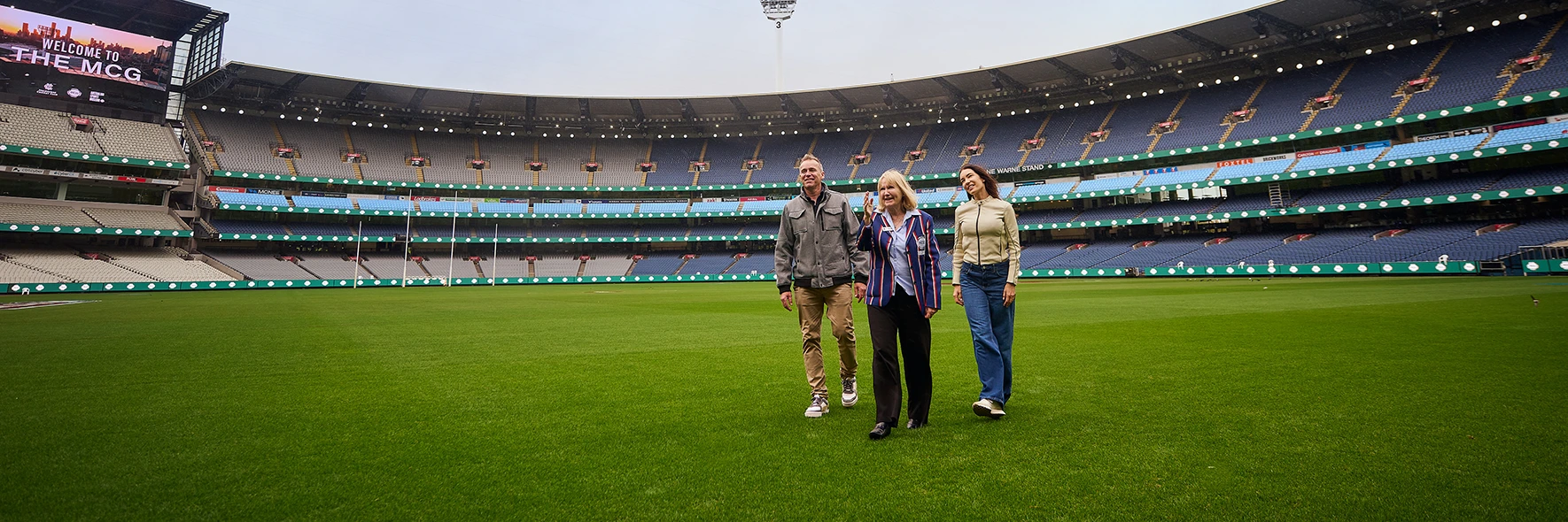 Group of 3 walks across the MCG turf during a stadium tour