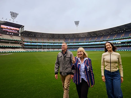 Group of 3 walks across the MCG turf during a stadium tour