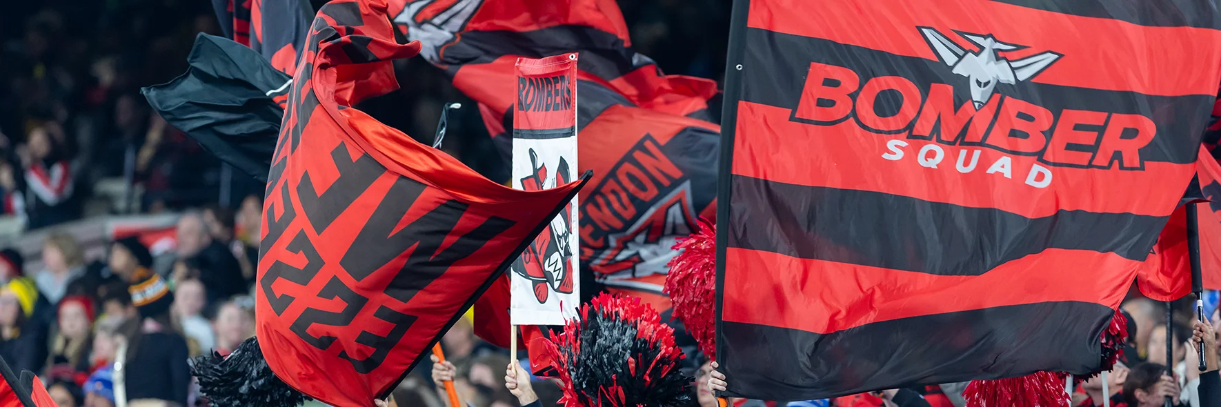 Essendon FC fans wave flags in the MCG stands after a goal