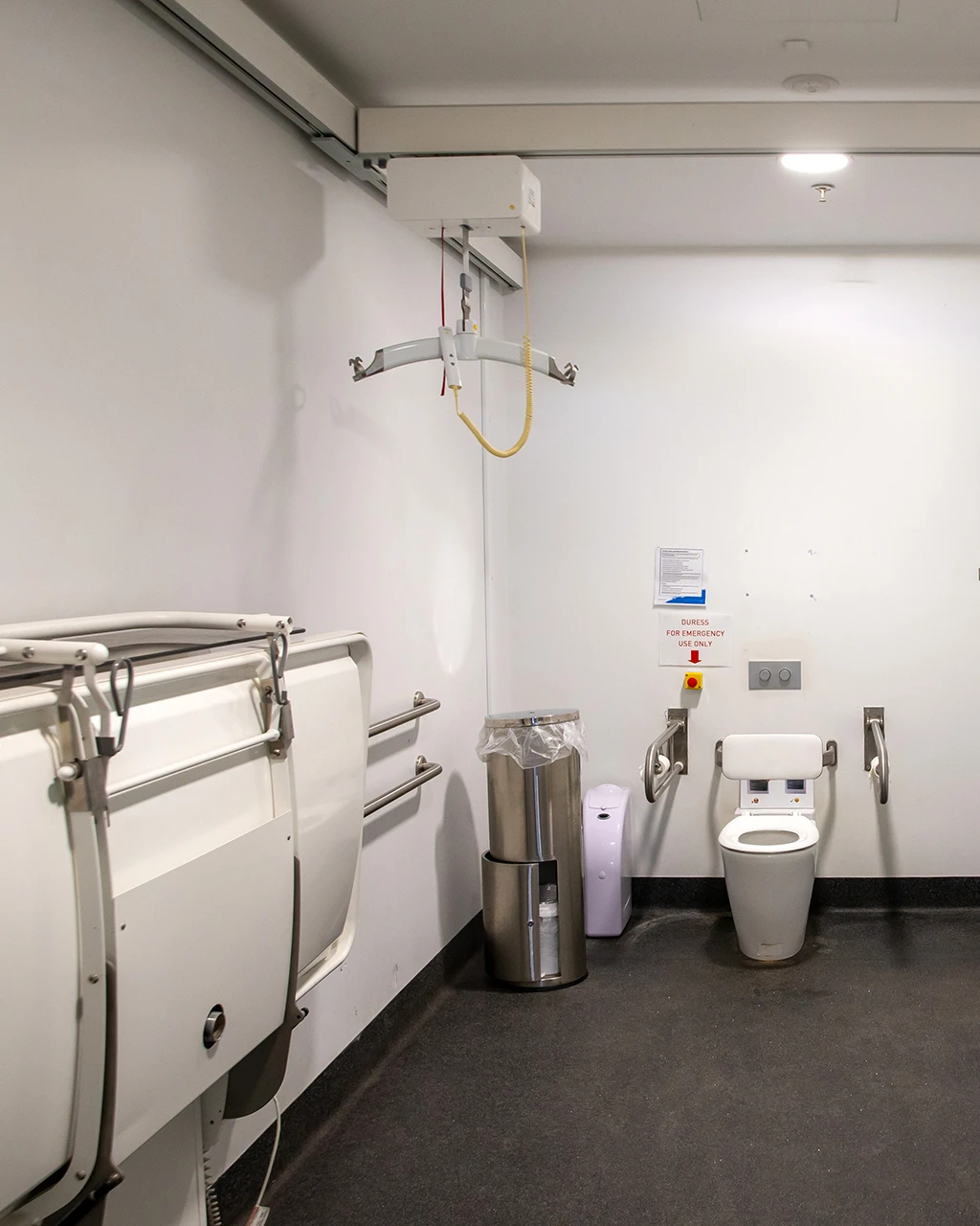 Inside a large bathroom with a ceiling hoist, adult-sized change table and toilet.