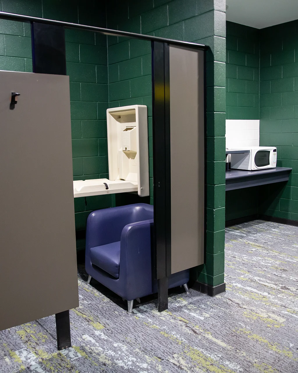 Carpeted room with microwave and private cubicle with baby change table and armchair.