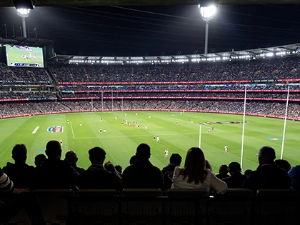 Spectators watching an AFL match at the MCG under lights at night
