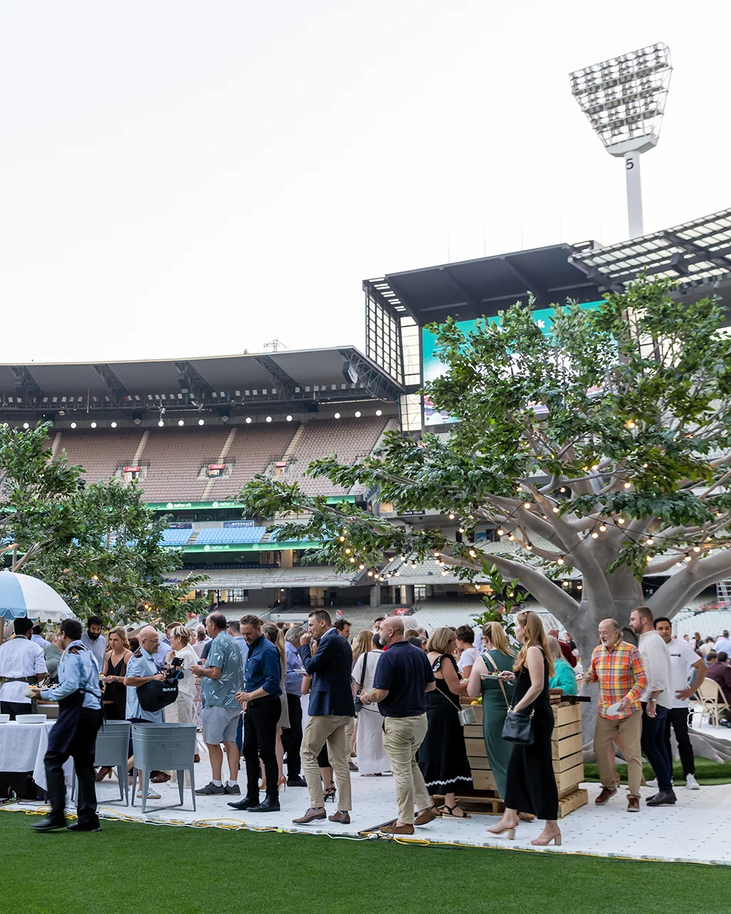 Guests at a function on the MCG arena. Trees and seats decorate the event, against the backdrop of the stadium