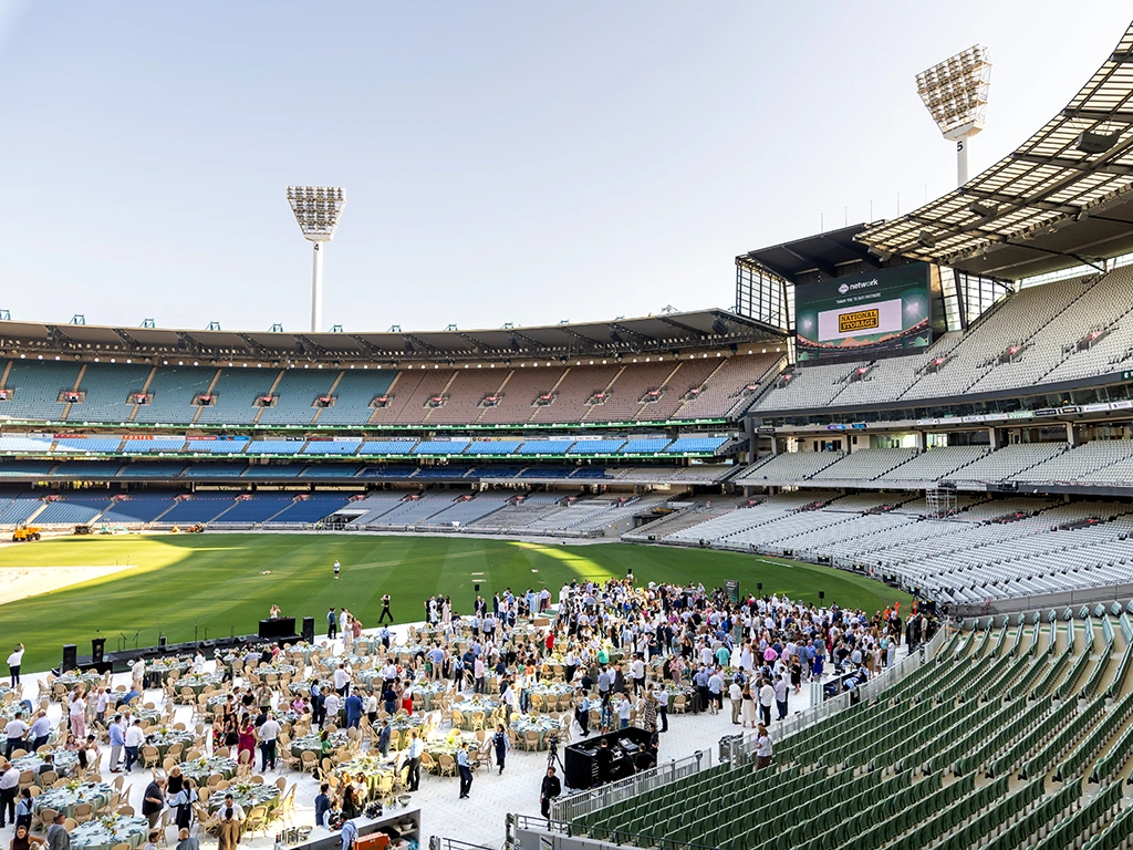 Guests mingle at a function on the MCG arena, with a backdrop of the seating bowl and sky