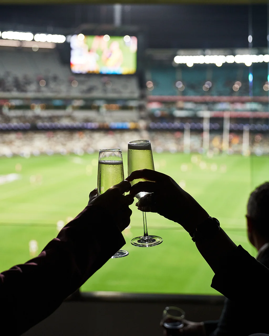 Champagne flutes with an AFL match in the background