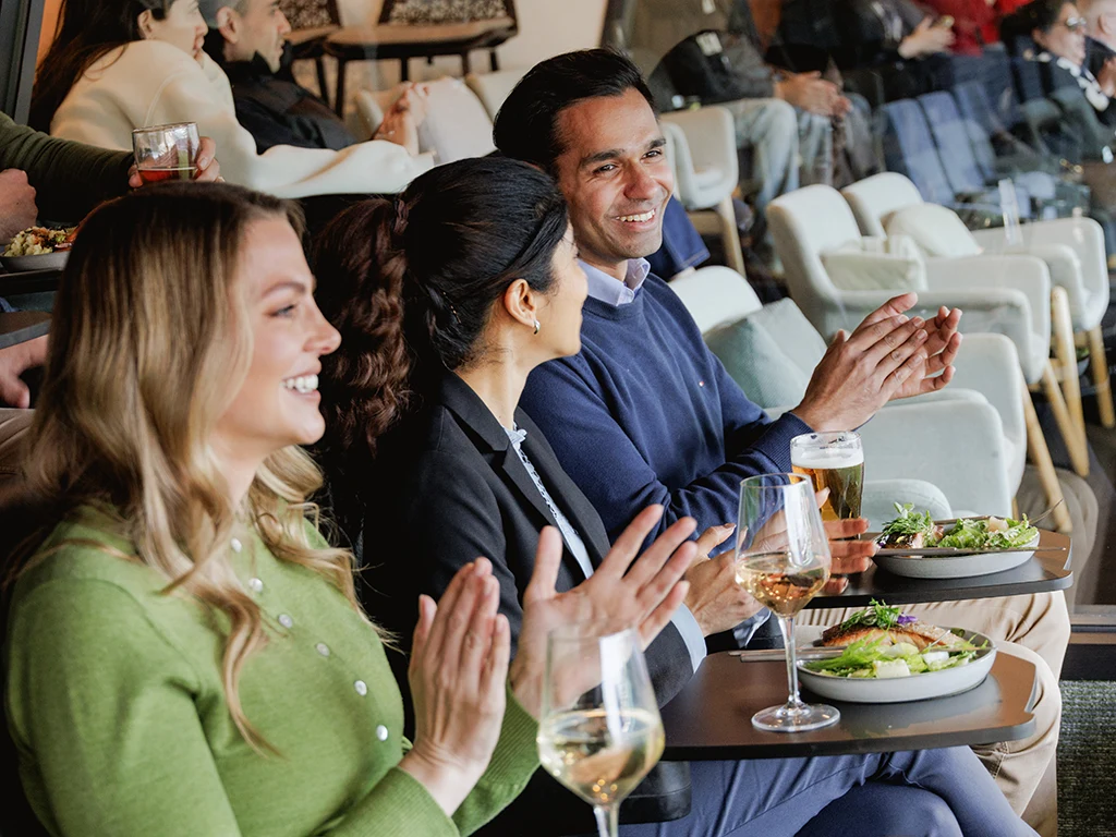 Guests enjoying drinks and food while cheering from suite at the MCG.
