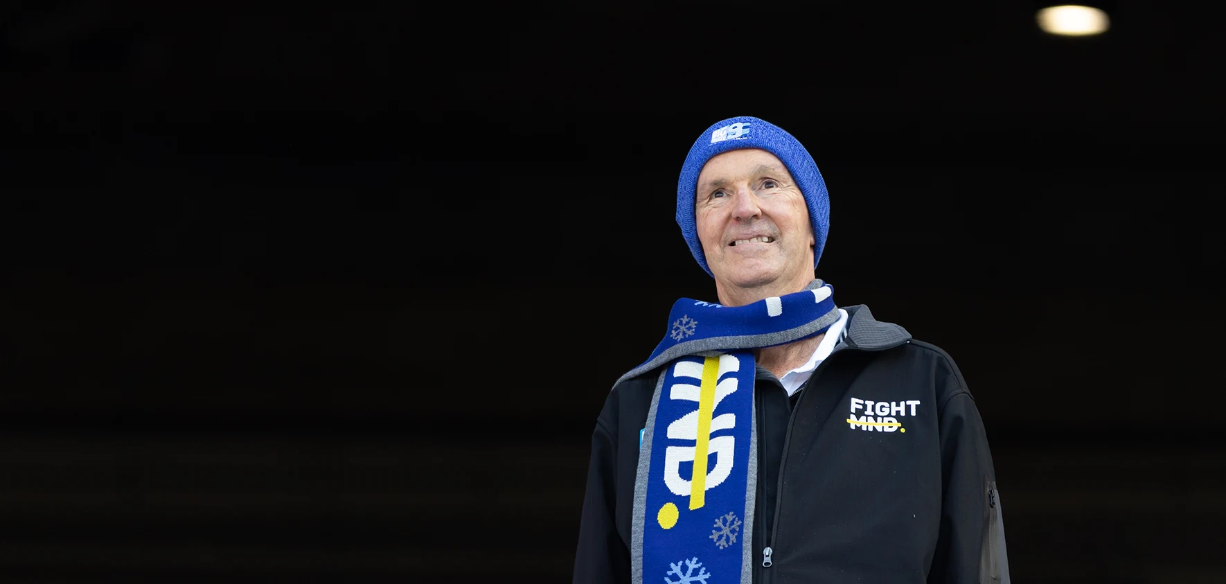 Neale Daniher smiles, wearing FightMND scarf and beanie