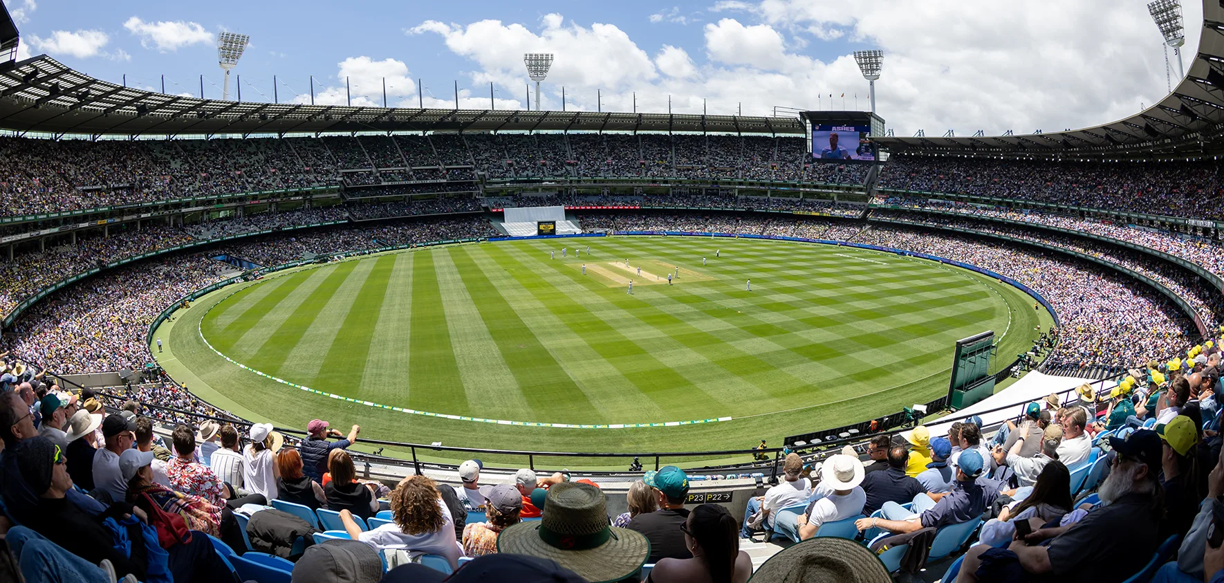 Packed MCG crowd watches Boxing Day Test cricket under blue skies.
